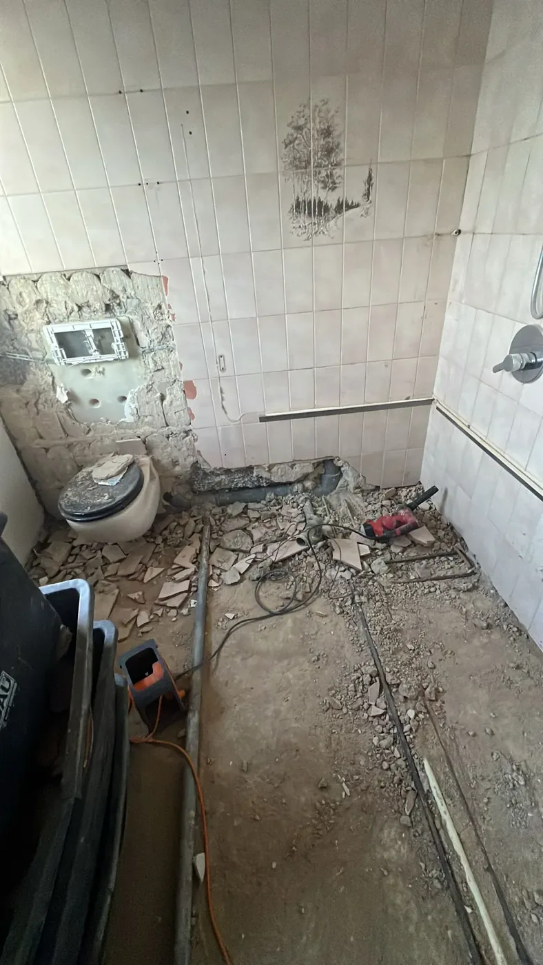 Bad in einem Reihenhaus im Rückbau mit abgeschlagenen Fliesen, freigelegtem Untergrund und offenen Leitungen