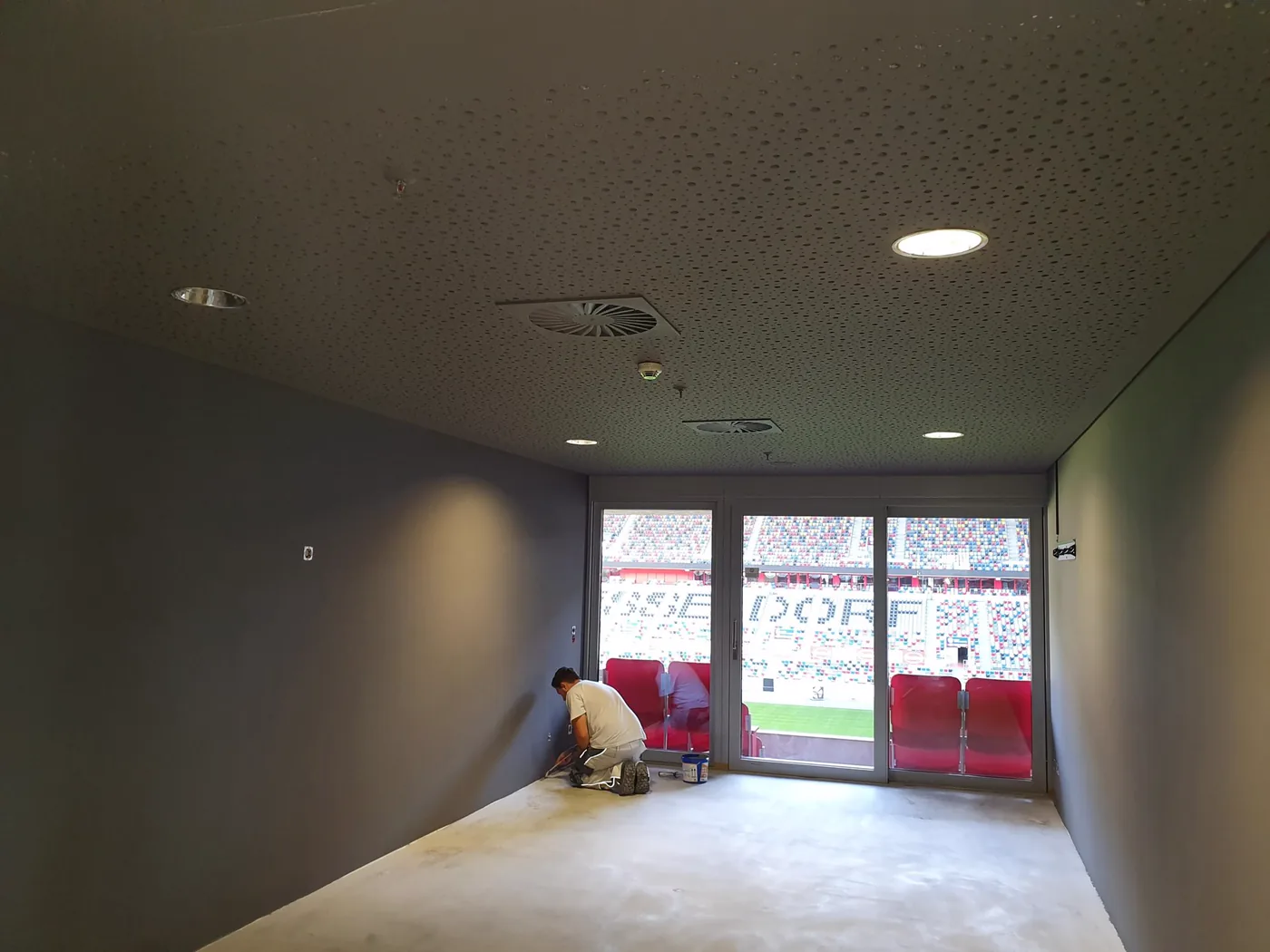 VIP-Lounge in der Sportstätte während der Ausführung, Wandflächen werden gespachtelt, Blick durch die Fensterfront auf die Tribüne