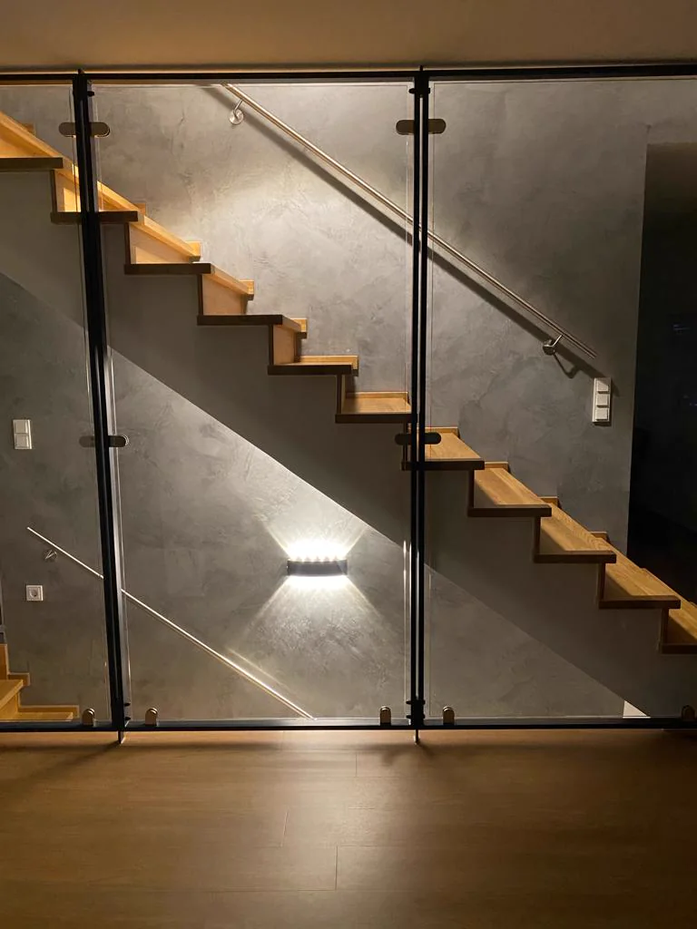 Handwerkliches Detail: Treppenaufgang mit Glasgeländer, Holz und beleuchteter Spachtelwand